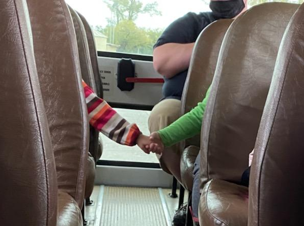 Two students holding hands across the school bus aisle 
